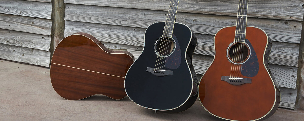 Three Yamaha L Series acoustic guitars against a weathered wooden wall.